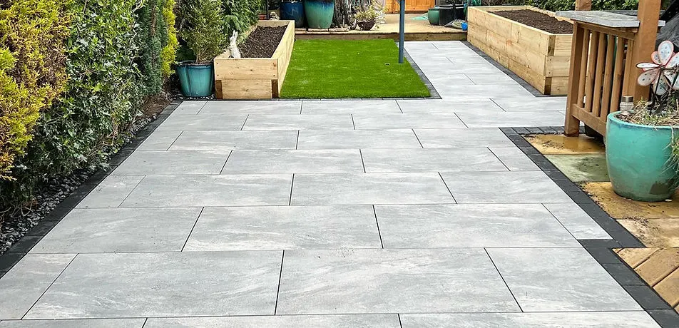 Precisely laid light porcelain patio with sleeper planters by JDS Landscaping