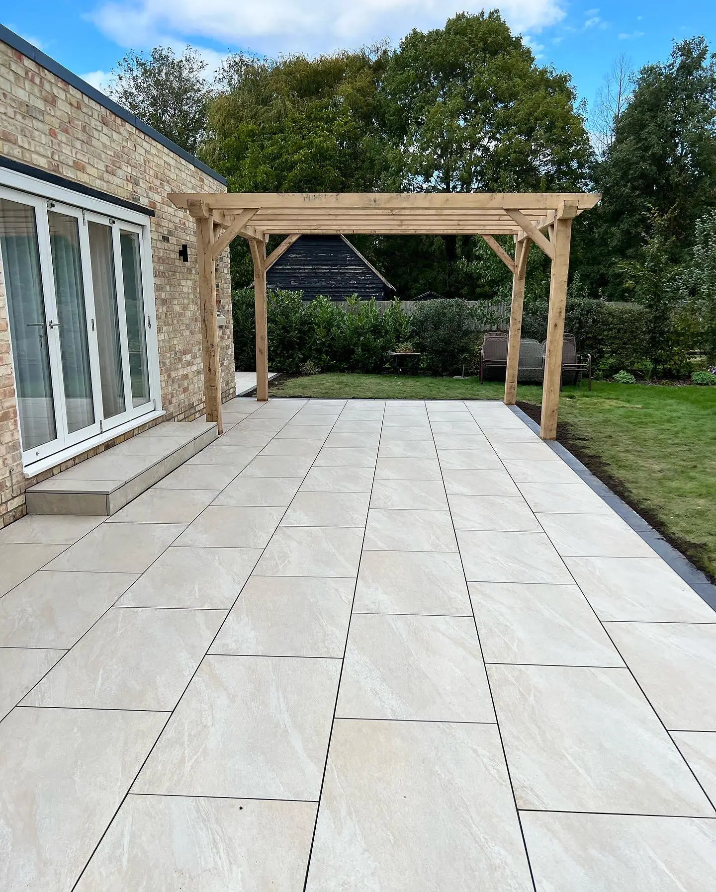 Light porcelain patio beneath a timber pergola by JDS Landscaping